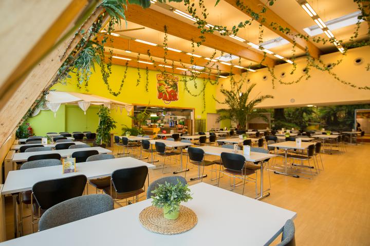 Helles Selbstbedienungsrestaurant mit Sitzplätzen und Blick auf die Indoor-Spielwelt des Monki Parks.